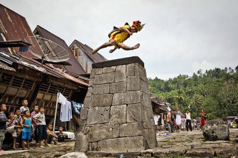 A villager wearing traditional costume jumps over a stone